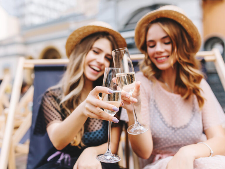 Outdoor portrait of cheerful young women celebrating with goblets of champagne
